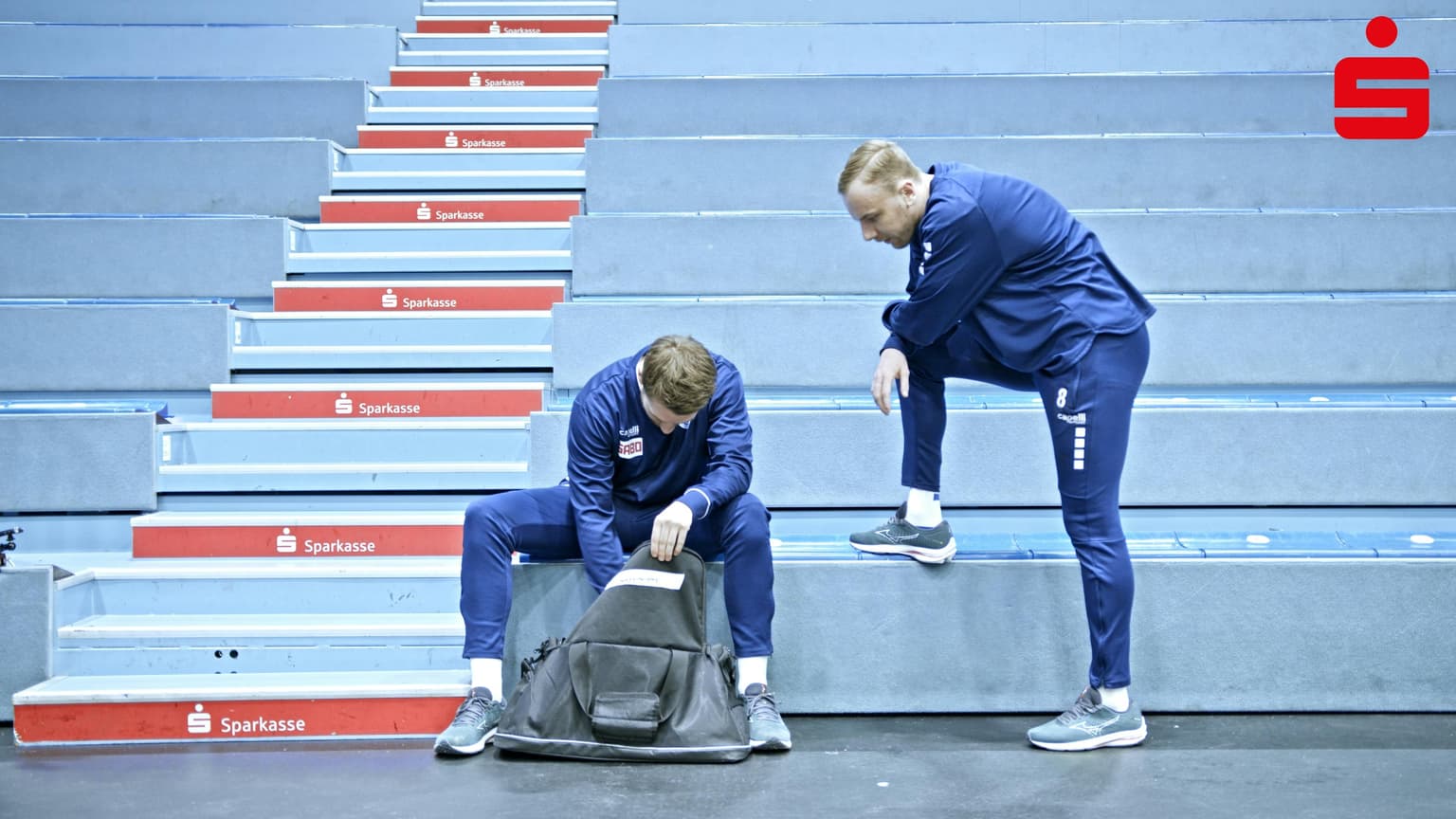 Zwei Männer in blau gekleidet auf der ersten Stufe einer Tribüne