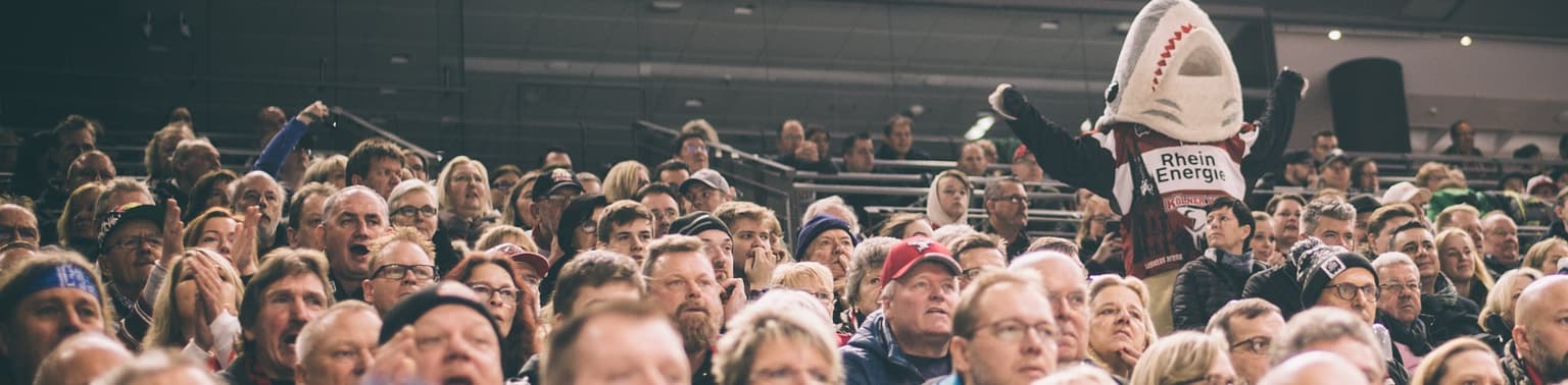 Sharky, das Maskottchen vom KEC Köln auf der Tribüne mit Fans. Emotional mit Höchstform Agency